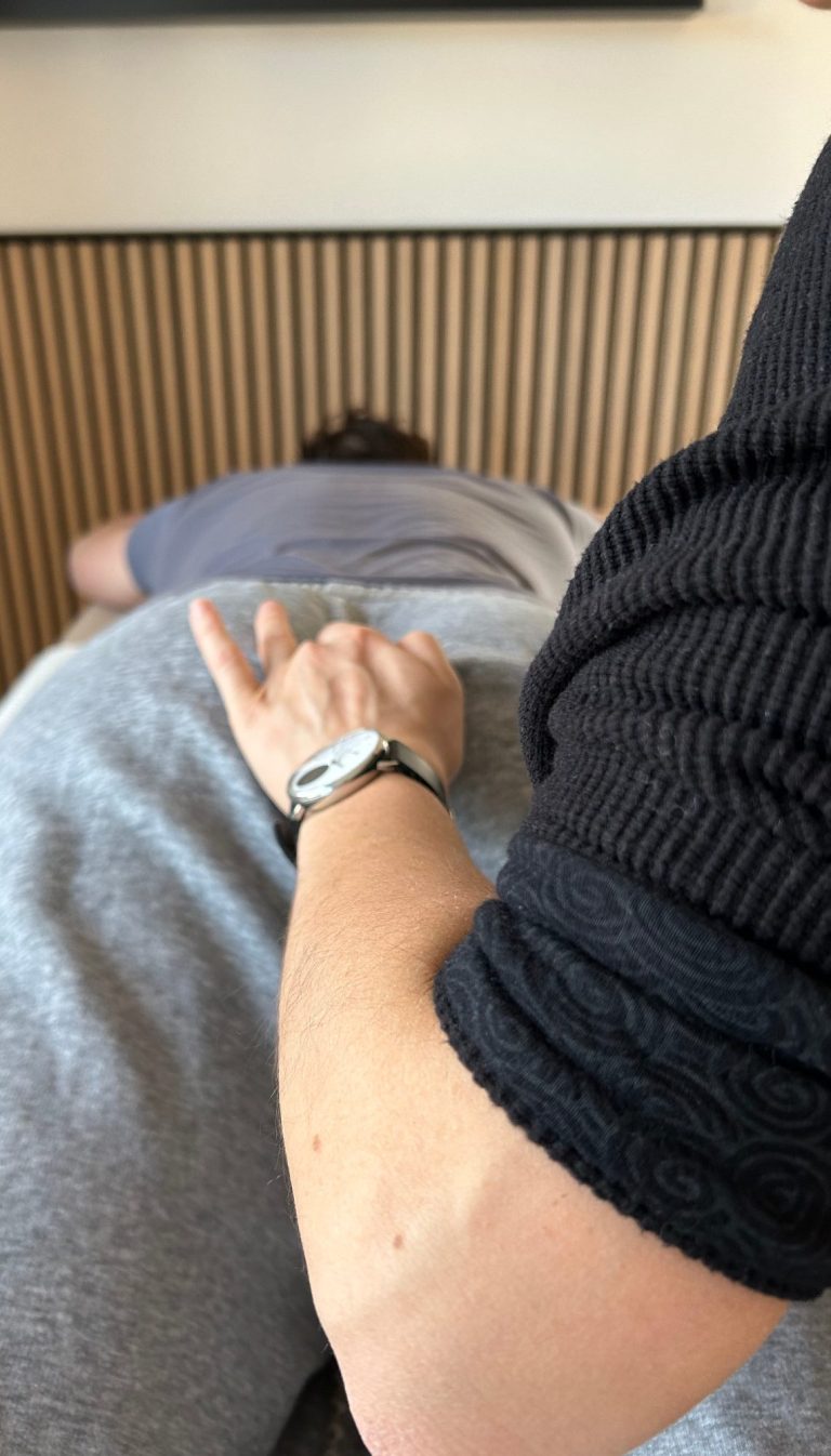 Franziskas Arm von hinten während sie Spinalflow gibt. Ihr Finger berührt einen Kontaktpunkt am Kreuzbein.